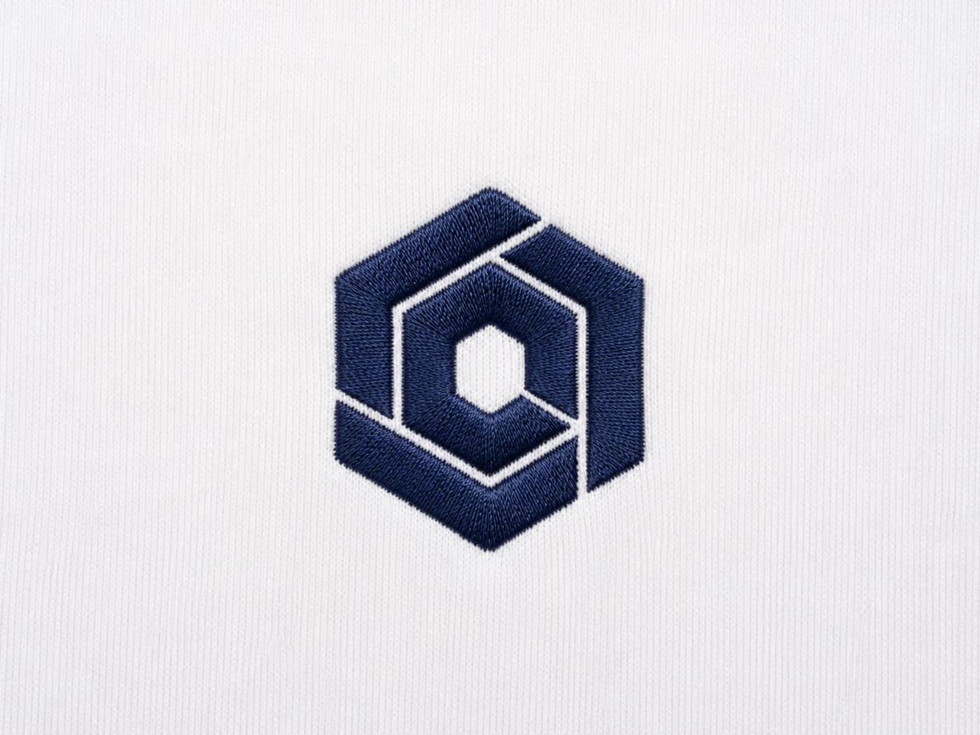 Macro d’un logo brodé marine sur maille de coton blanche, fil dense et intact